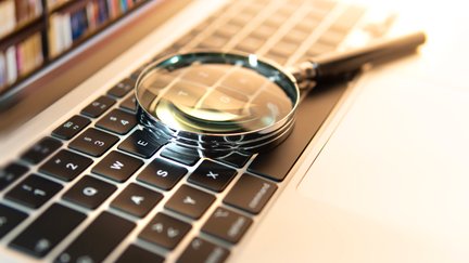 Lupe, die auf einer Laptop-Tastatur liegt und Bücherregal auf dem Bildschirm  