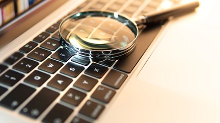 Lupe, die auf einer Laptop-Tastatur liegt und Bücherregal auf dem Bildschirm  