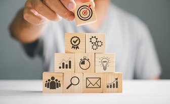 Pyramidenförmig von einer Person aufgestapelte Holzblöcke, auf denen unterschiedliche Symbole abgebildet sind    