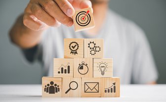 Pyramidenförmig von einer Person aufgestapelte Holzblöcke, auf denen unterschiedliche Symbole abgebildet sind    